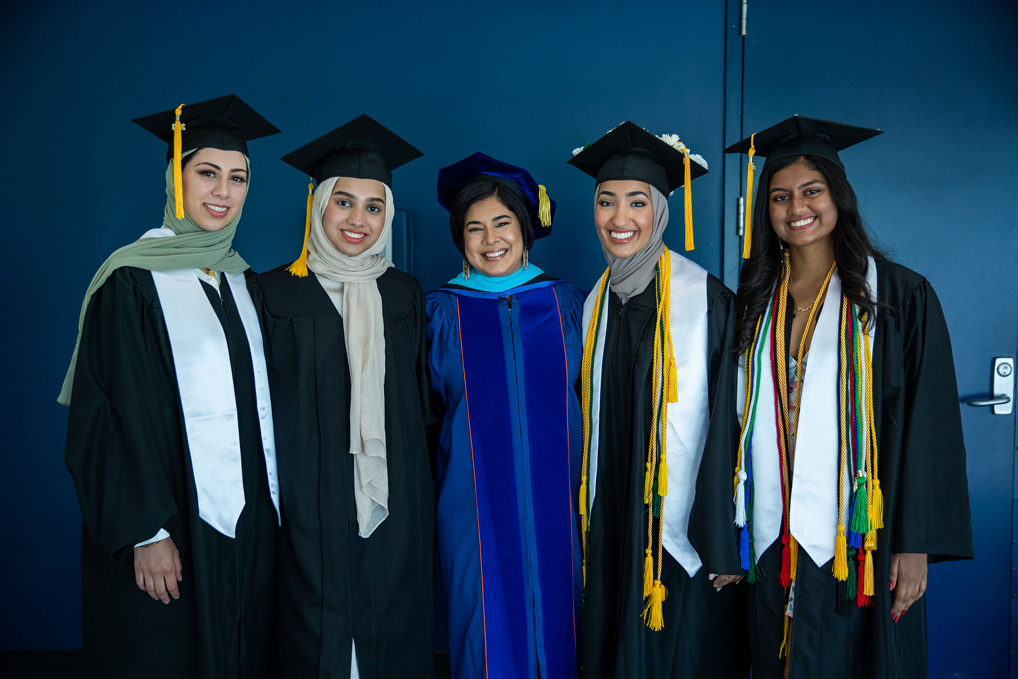 Seher Awan posing with 4 female graduates in their commencement robes