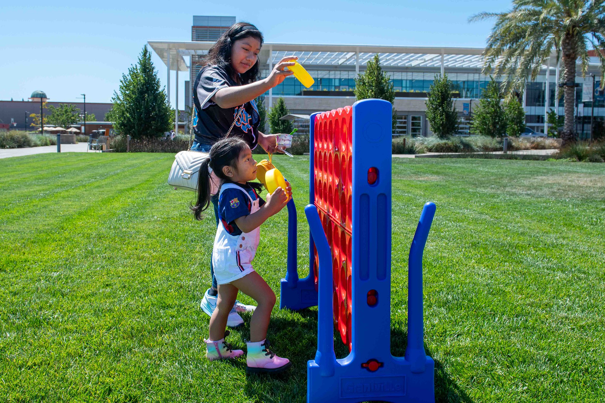 Member of EOPS playing extra large Connect4 game outside with child