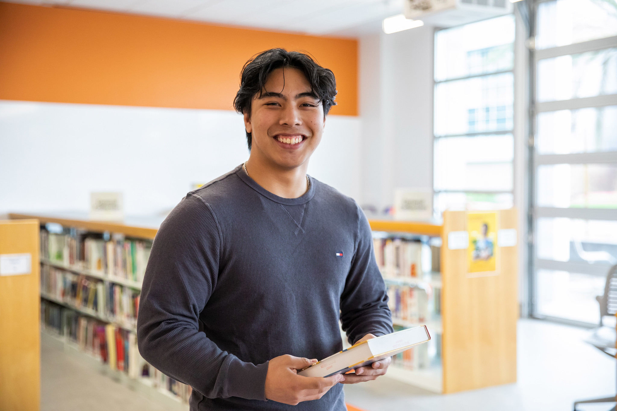 Mission College student smiling holding a book in the library