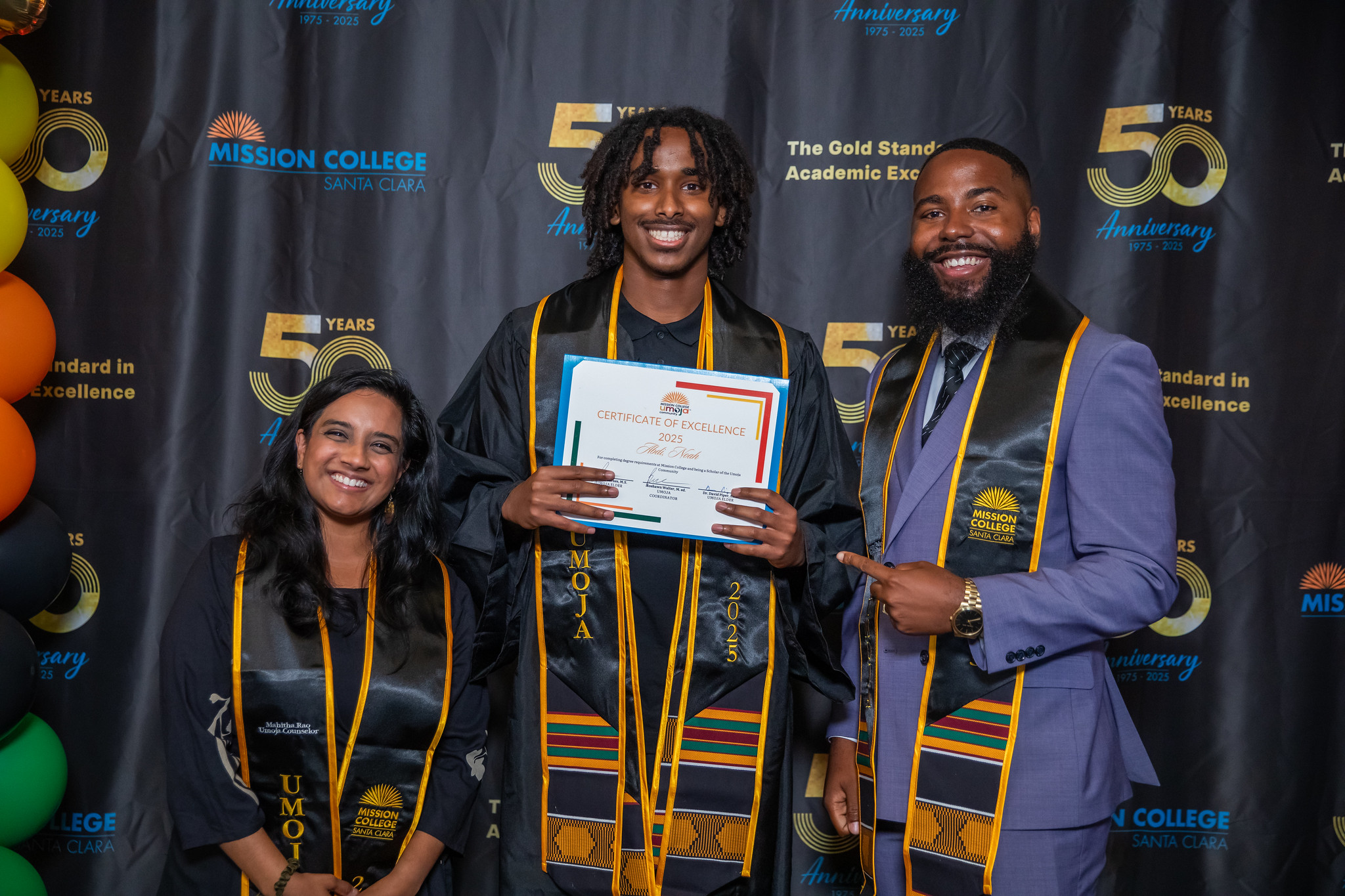 Umoja grad holding certificate next to two faculty members