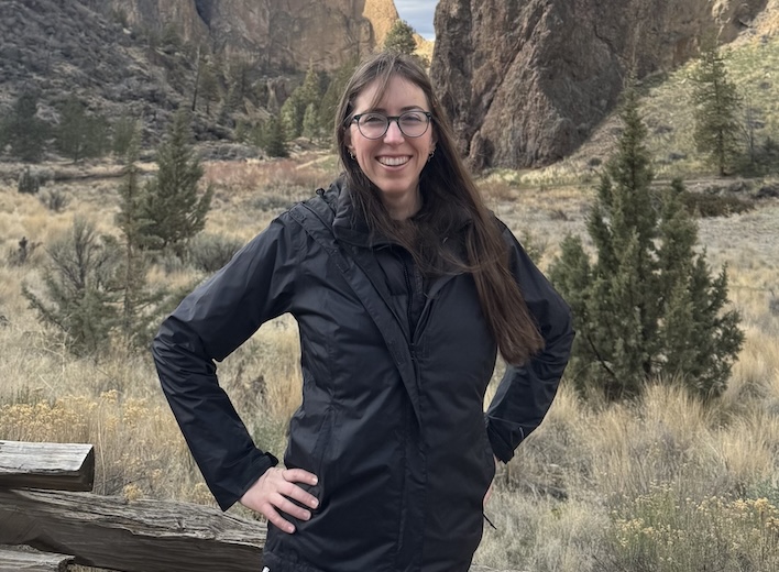 Brittany Gunnel, a white woman with long brown hair poses in front of large rocks in the desert.