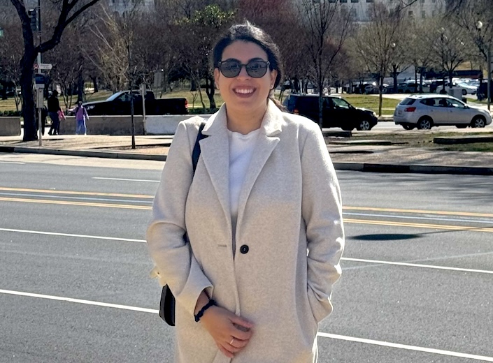 Priscilla de franco-moreira stands in front of the California State Capital. She wears a white peacoat and has her dark hair pulled back.